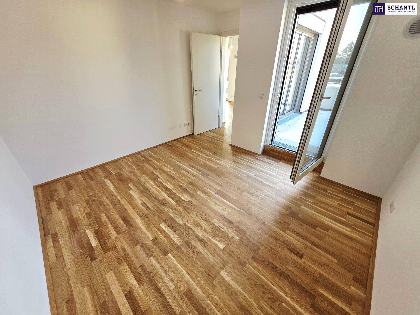 Leeres Zimmer mit Holzboden und offener Balkontür, die den Zugang zum Außenbereich ermöglicht.