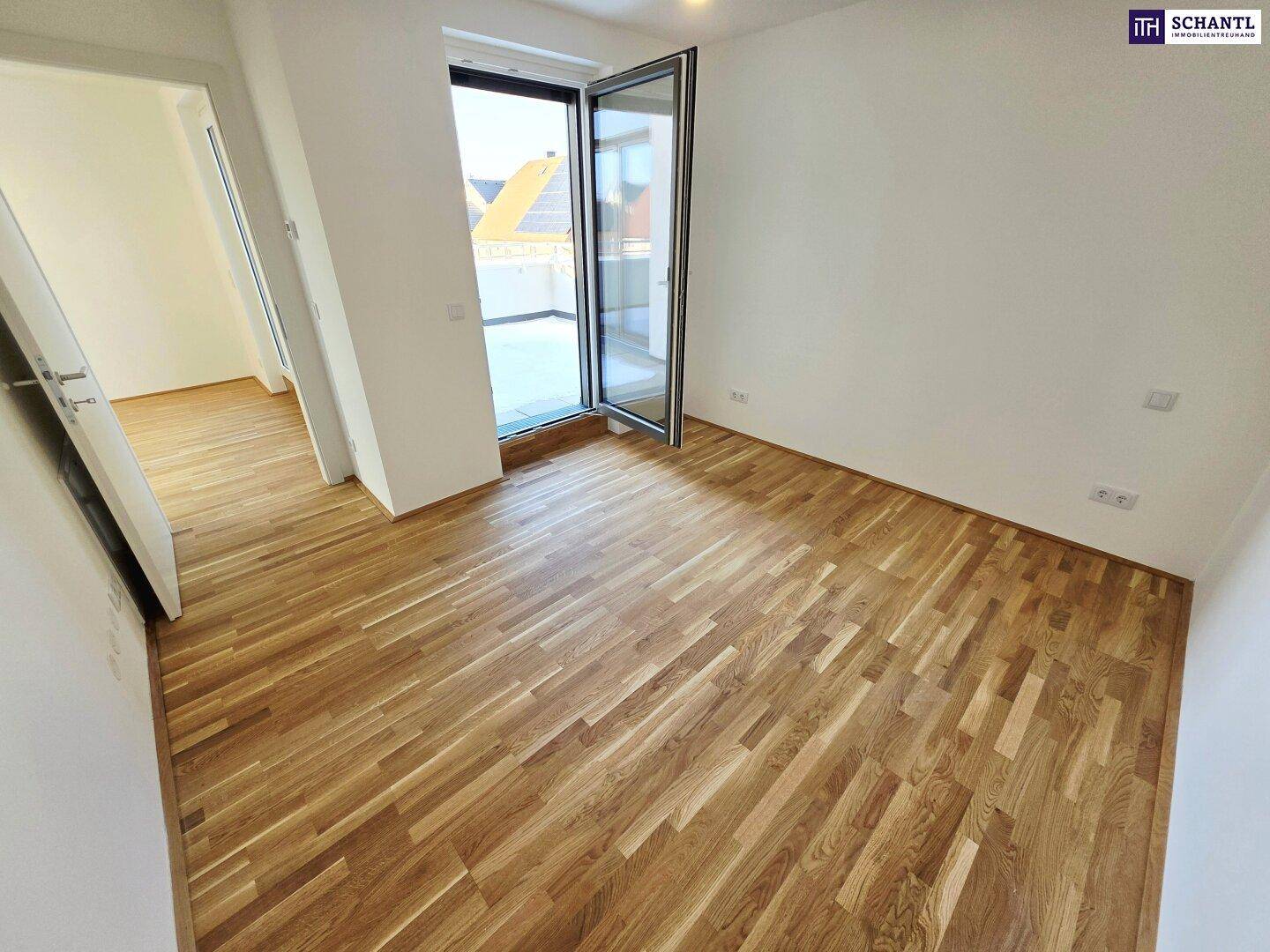 Leeres Zimmer mit Holzboden und offener Tür zum Außenbereich, das viel Licht empfängt.