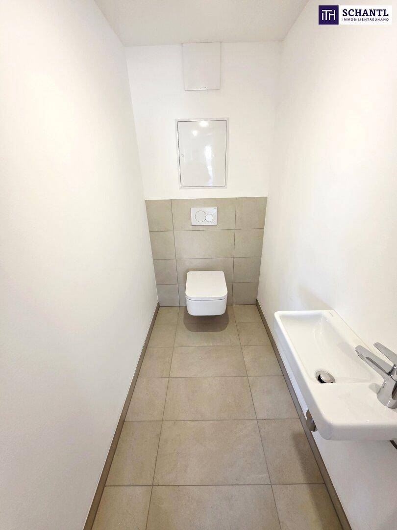 Separate Gästetoilette mit Wand-WC, kleinem Waschbecken und hellen Fliesen.
