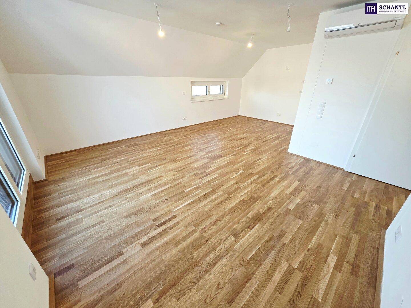 Unmöbliertes Zimmer mit Parkettboden, Dachschrägen und einem kleinen Fenster.