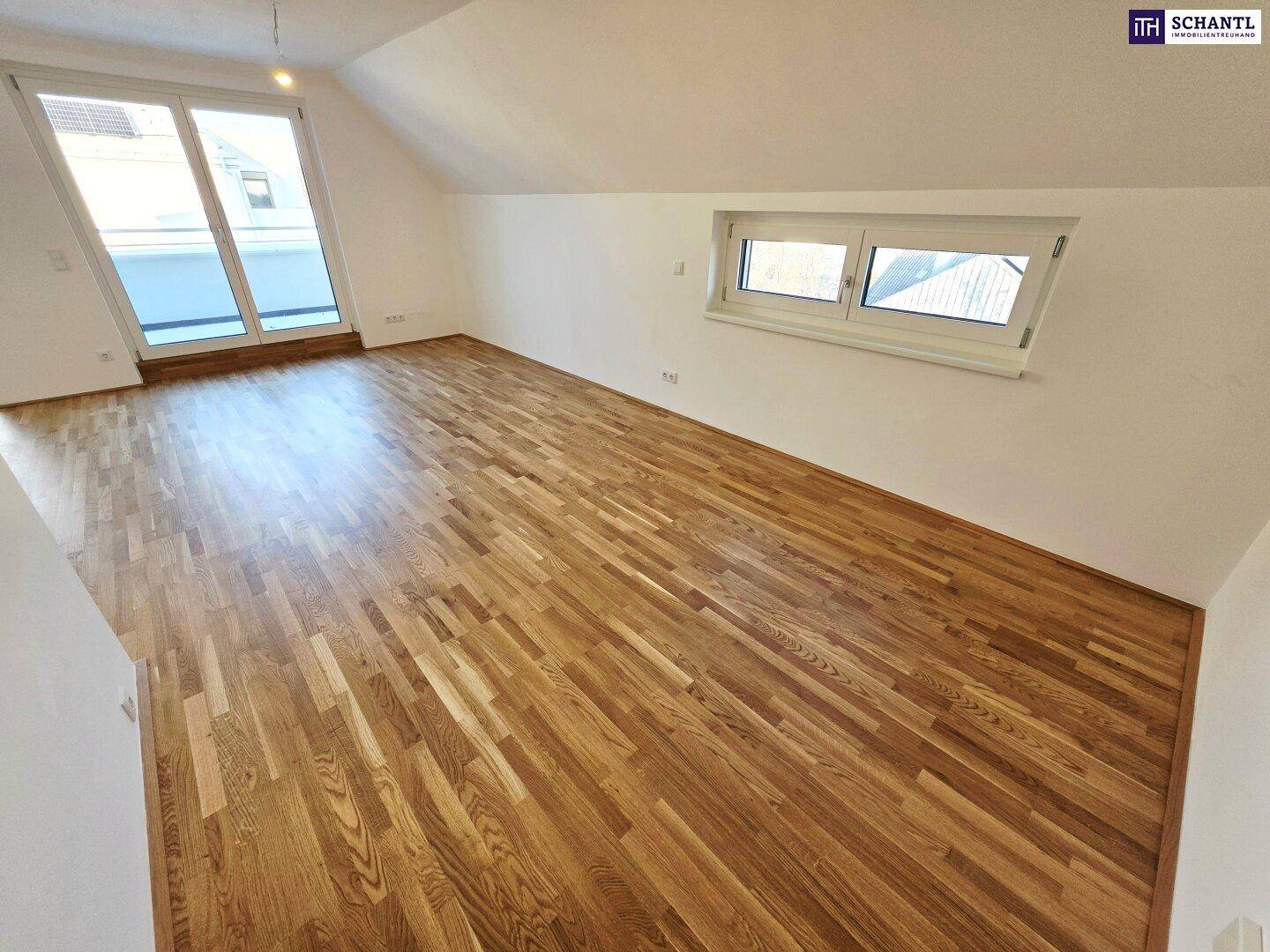Geräumiges Zimmer mit Holzboden und viel Tageslicht durch die Fensterfront und Dachfenster.