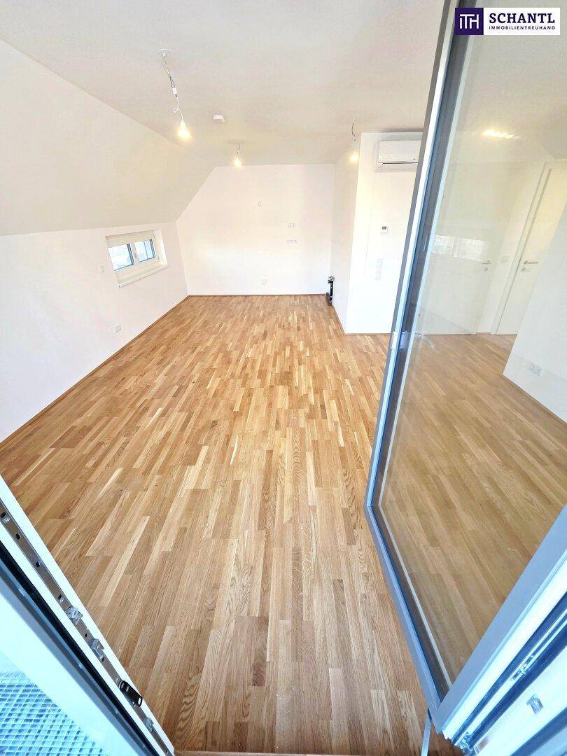 Helles Zimmer mit Parkettboden, Dachschrägen und Blick durch die offene Balkontür.
