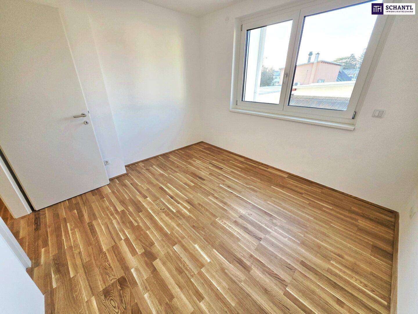 Helles Schlafzimmer mit Parkettboden und Fenster, das viel Tageslicht hereinlässt.