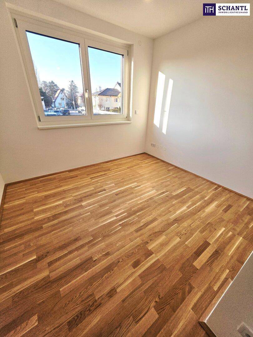 Helles Zimmer mit Parkettboden und Fenster, das einen Blick auf die Nachbarschaft ermöglicht.