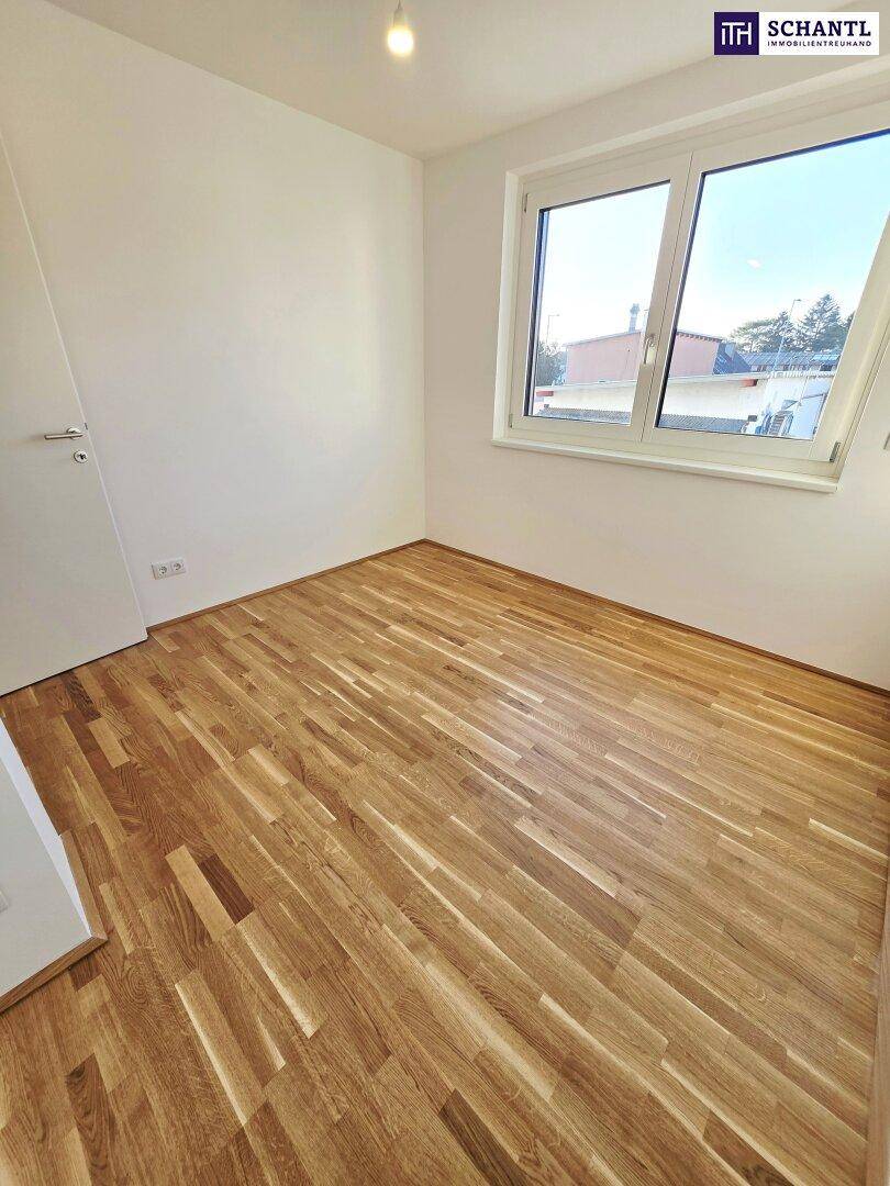 Helles Zimmer mit Parkettboden und großem Fenster, das viel Tageslicht hereinlässt.