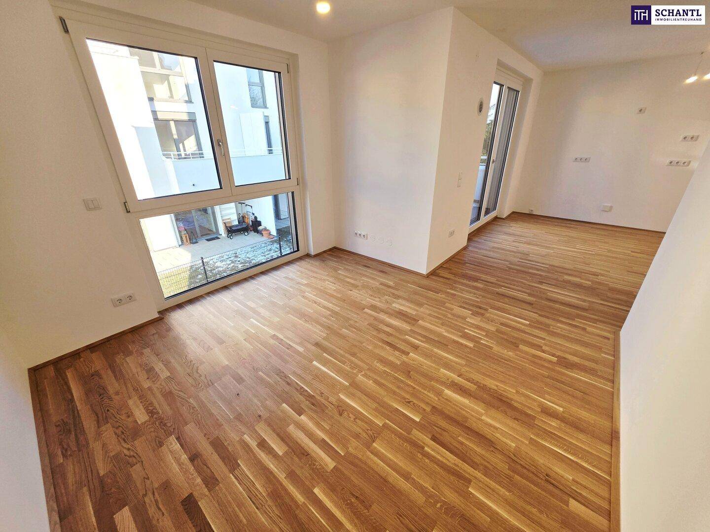 Geräumiges Wohnzimmer mit großen Fenstern und hellem Parkettboden, bereit zur Einrichtung.