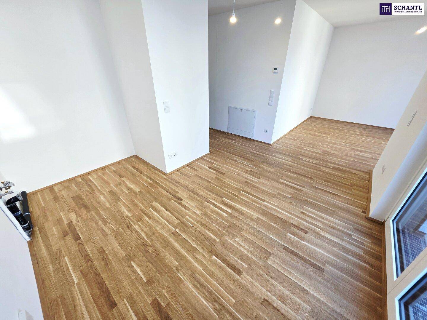 Heller Wohnbereich mit Parkettboden und großen Fenstern, die viel Licht hereinlassen.