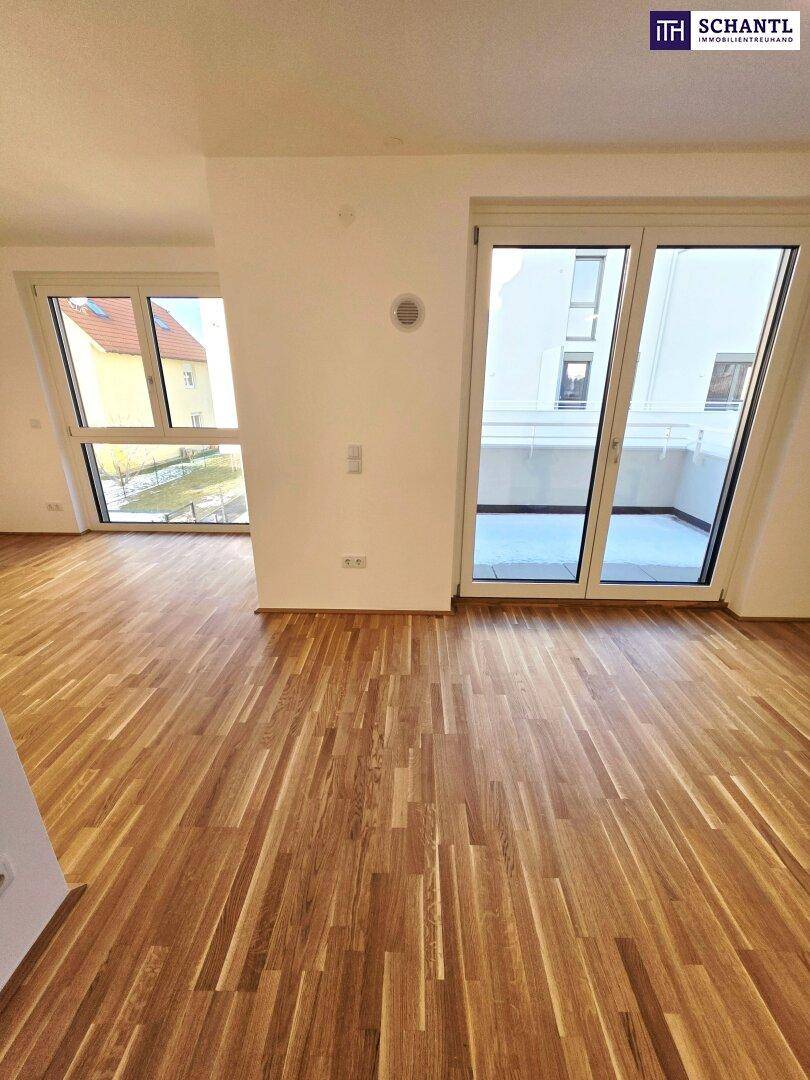 Geräumiger Wohnbereich mit Parkettboden und großen Fenstern, die viel Licht hereinlassen.