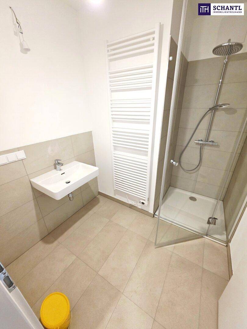 Modernes Badezimmer mit Dusche, Waschbecken und beheiztem Handtuchhalter in hellen Farbtönen.