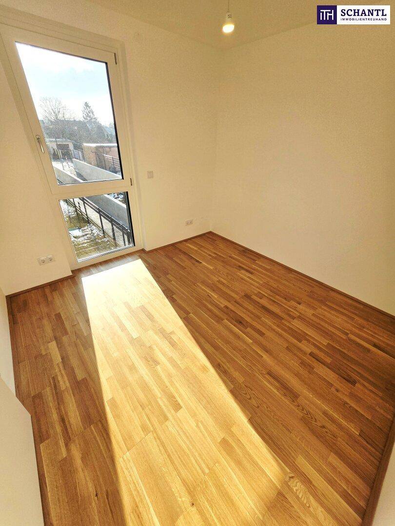 Sonniger Raum mit Parkettboden und Fenster, das einen Blick nach draußen bietet.