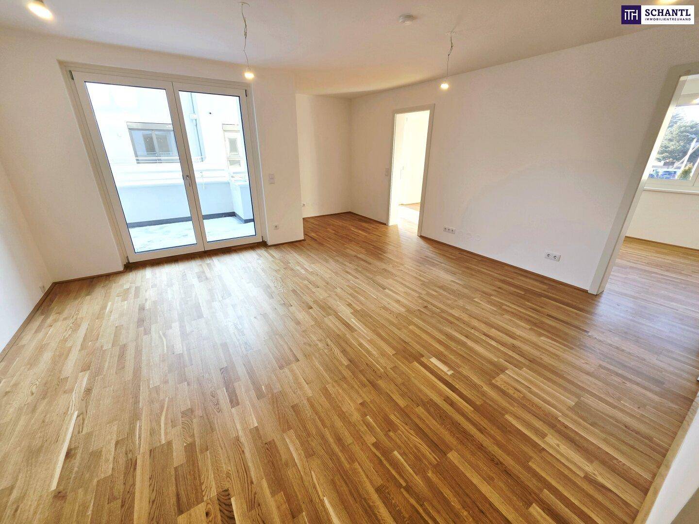 Geräumiger Wohnbereich mit hellem Parkettboden und Zugang zu einem Balkon.