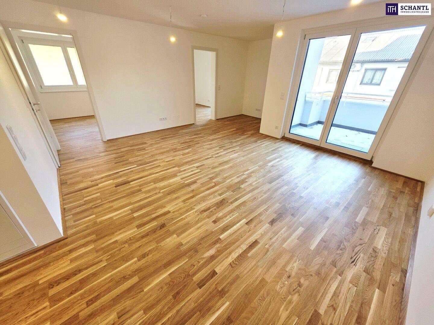 Geräumiger Wohnbereich mit hellem Parkettboden und großem Fenster mit Balkonzugang.