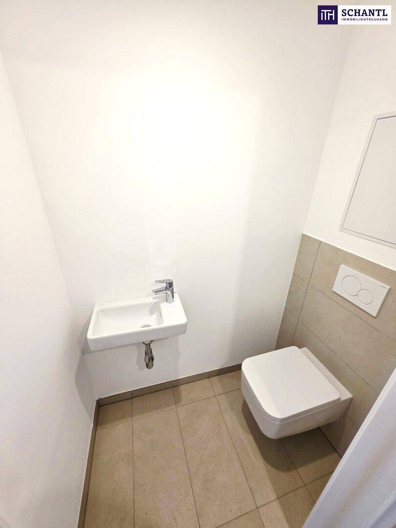 Gäste-WC mit wandhängender Toilette, kleinem Waschbecken und Fliesenboden.