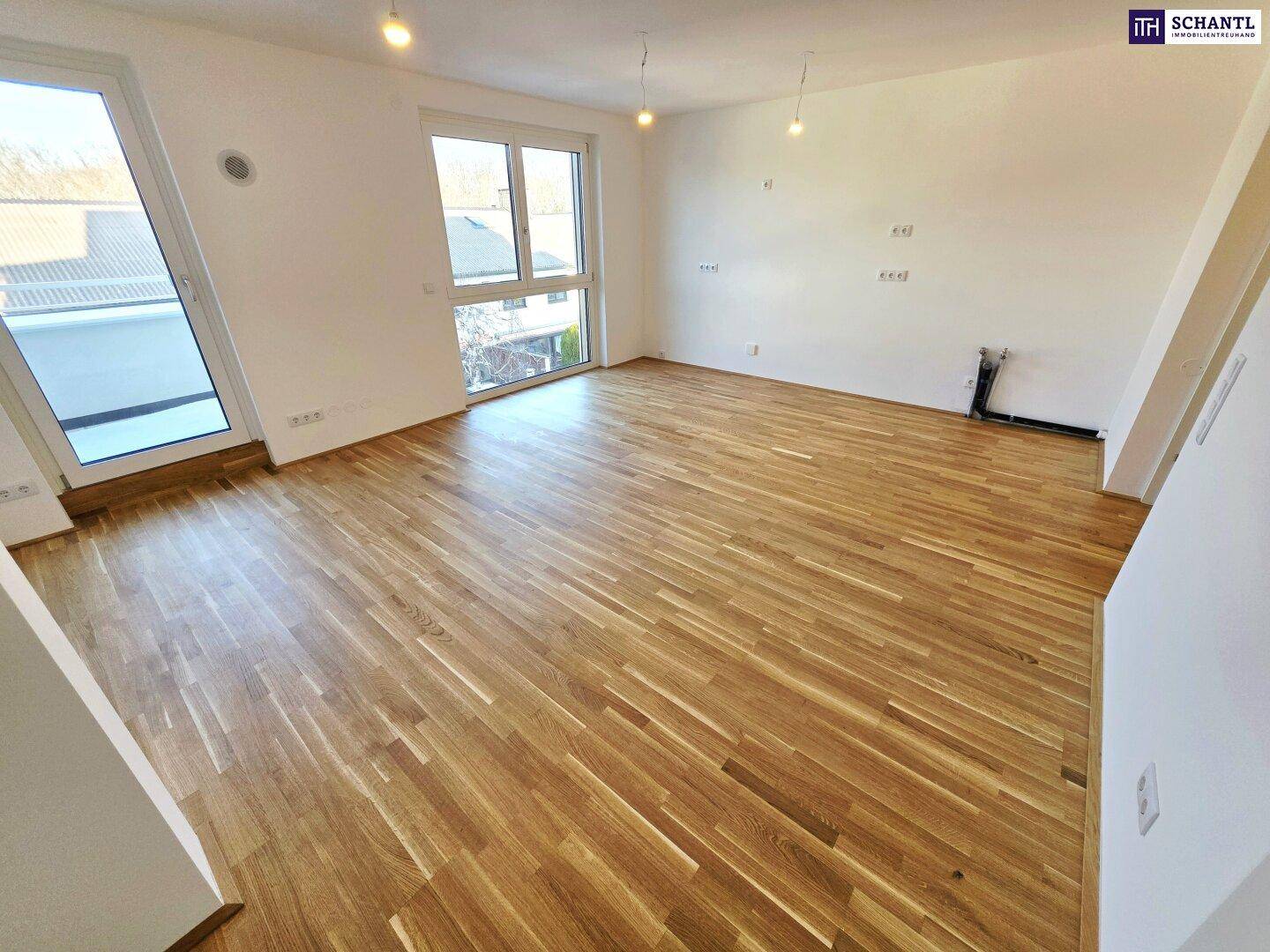 Geräumiger Wohnbereich mit hellem Parkettboden und großen Fenstern für viel Lichteinfall.