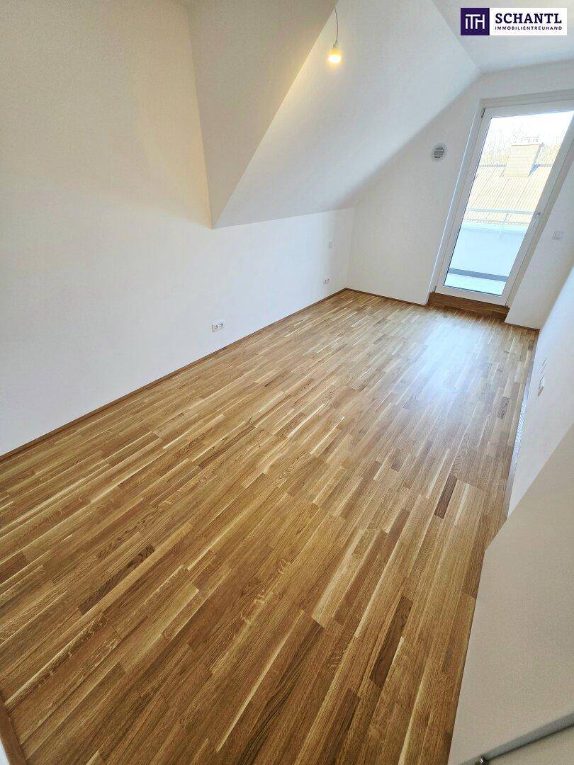 Dachgeschosszimmer mit schräger Decke, Parkettboden und großem Dachfenster.