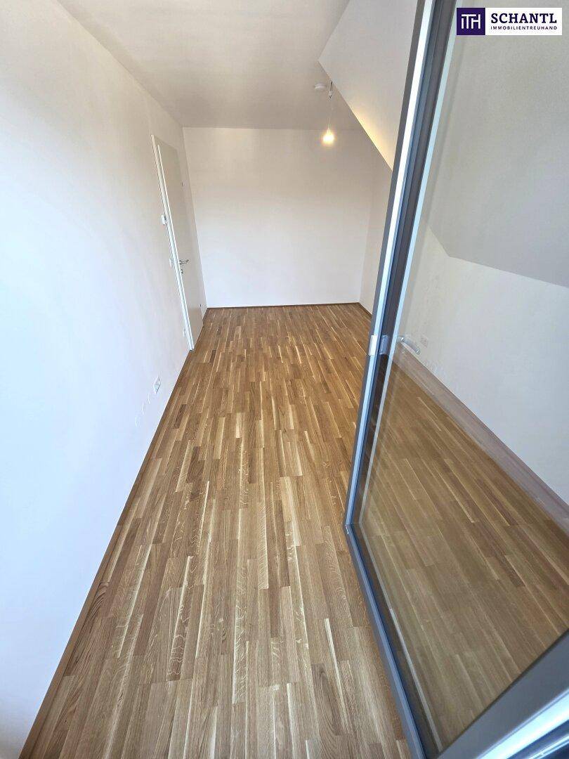 Langer, schmaler Raum mit Parkettboden und einer Tür, die nach draußen führt.