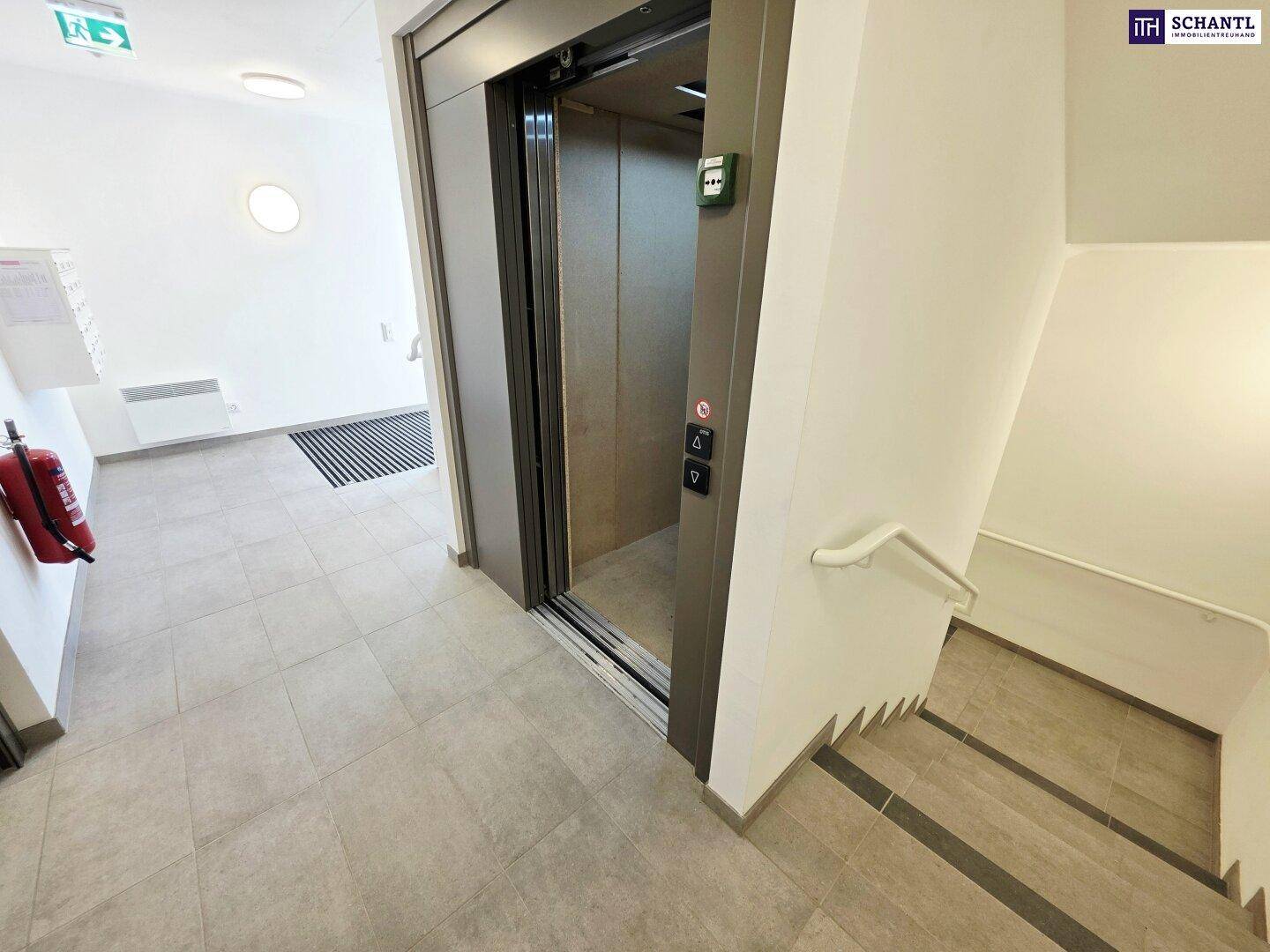 Eingangsbereich mit modernem Aufzug, Treppenhaus und Fliesenboden.