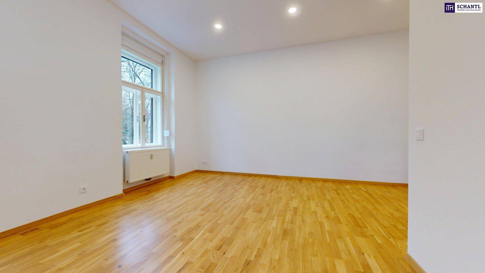 Geräumiges, helles Zimmer mit Holzboden und großem Fenster, ideal als Wohnbereich.