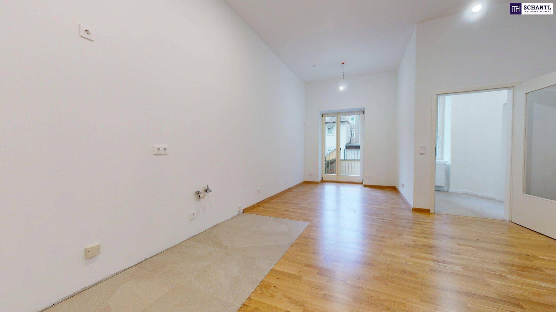 Heller Raum mit Holzboden und Fliesenbereich, vorbereitet für eine Küche mit Balkonzugang.