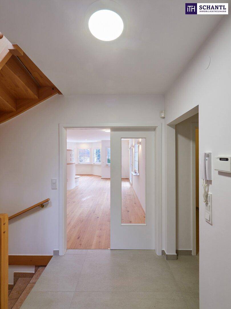 Heller Flur mit Fliesenboden und Blick in den Wohnbereich durch eine Glastür.