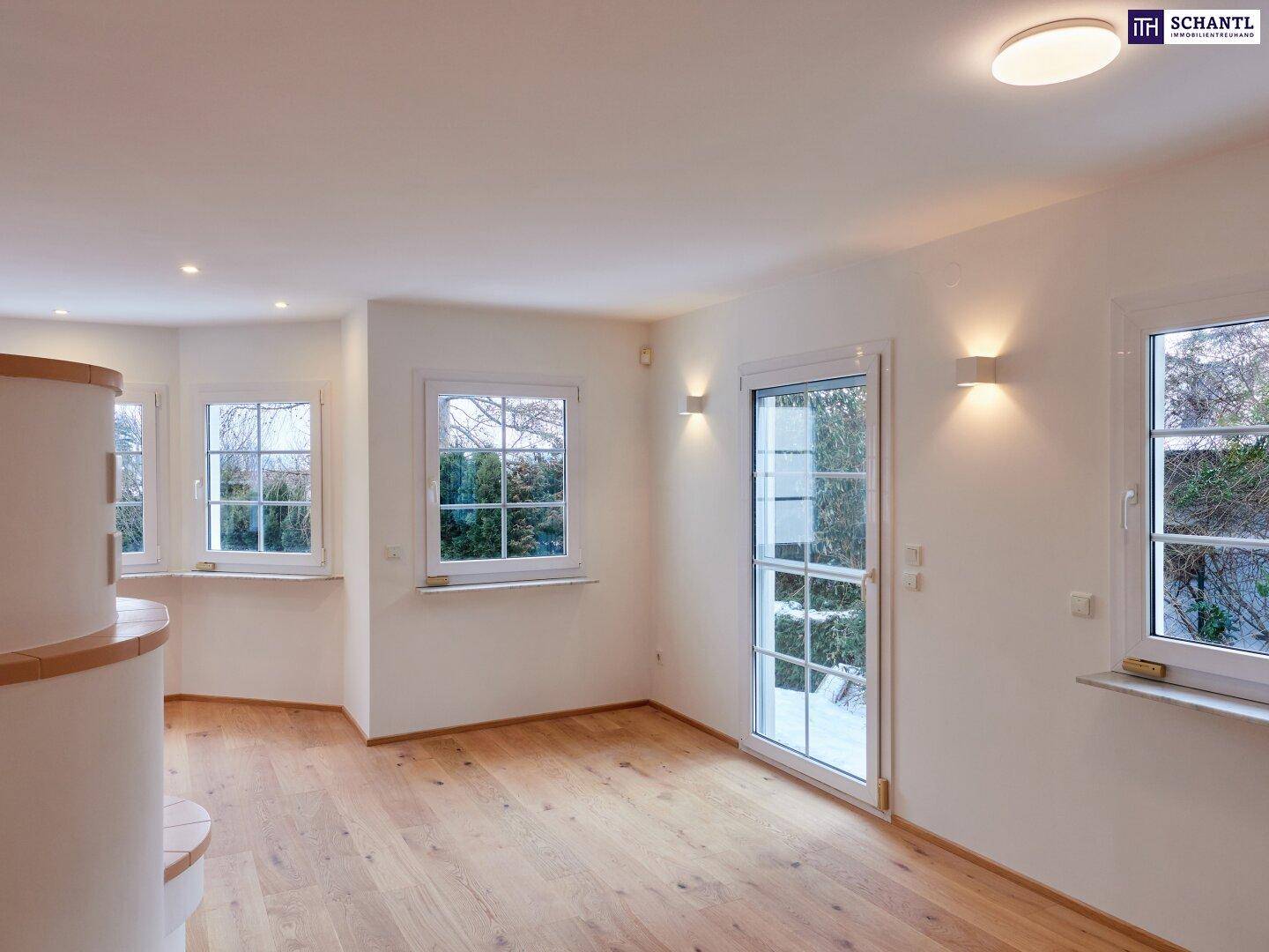 Lichtdurchfluteter Wohnraum mit Holzboden und mehreren Fenstern, die viel Tageslicht hereinlassen.