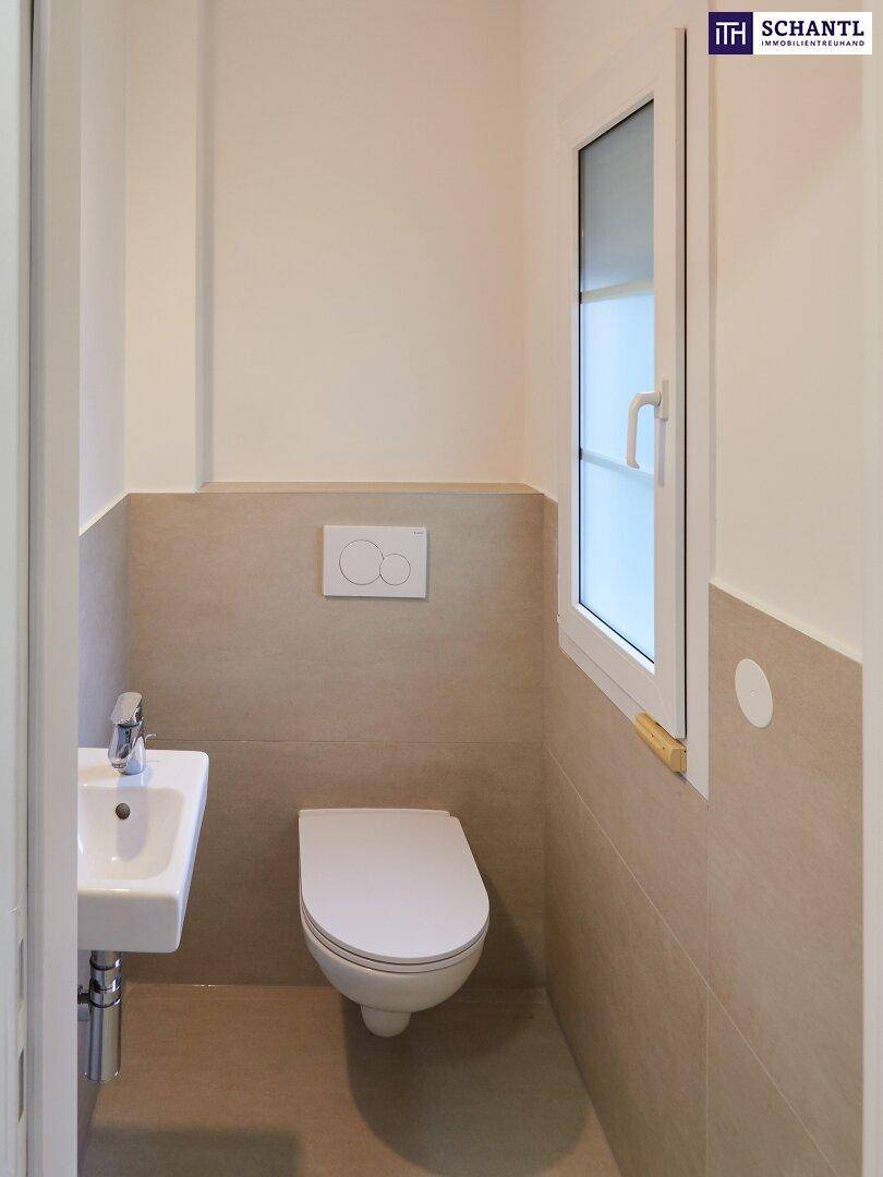 Modernes Gäste-WC mit Wand-WC, kleinem Waschbecken und Fenster für natürliche Belüftung.