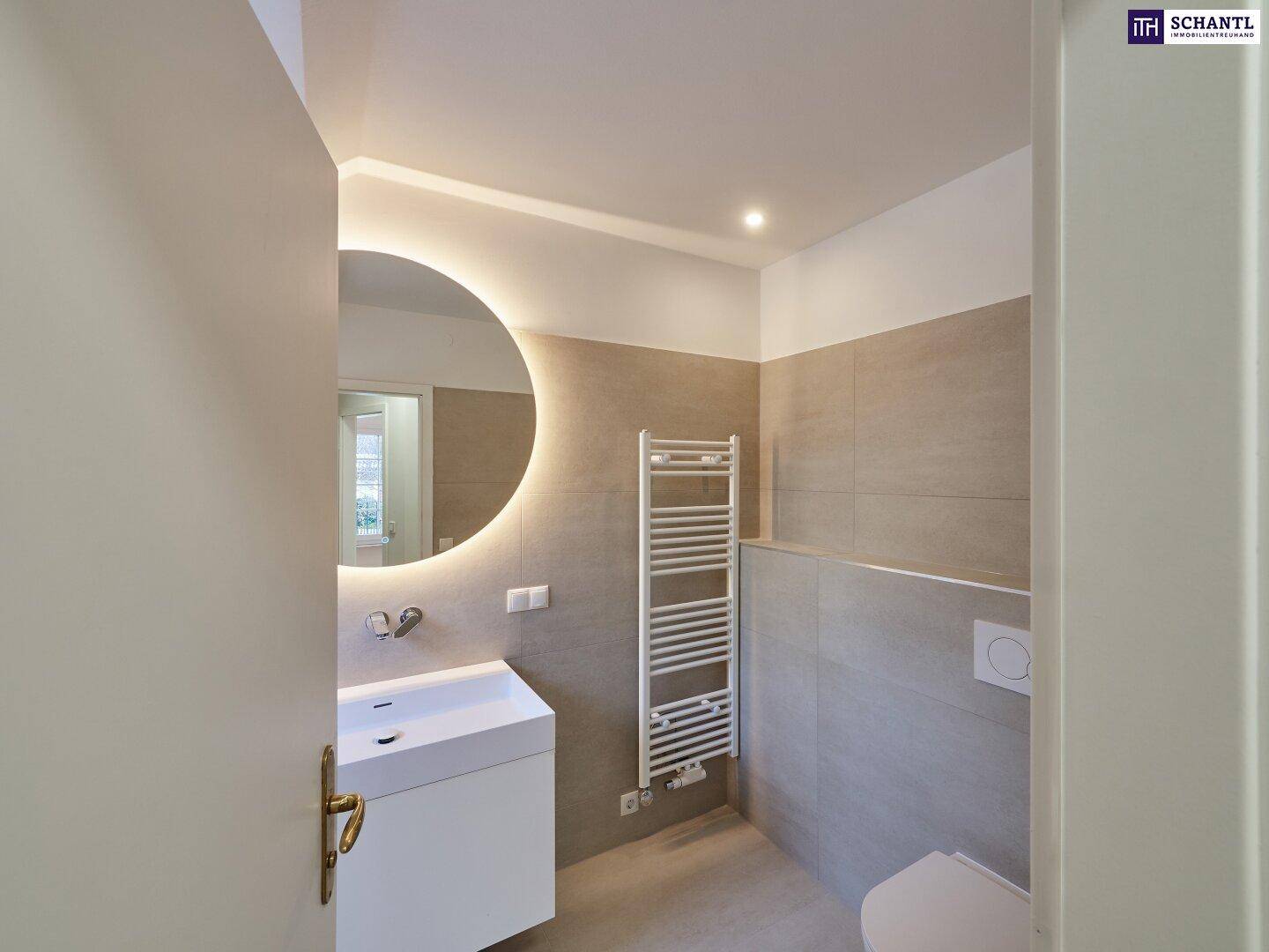 Modernes Badezimmer mit Waschtisch, beleuchtetem Spiegel und beheiztem Handtuchhalter.