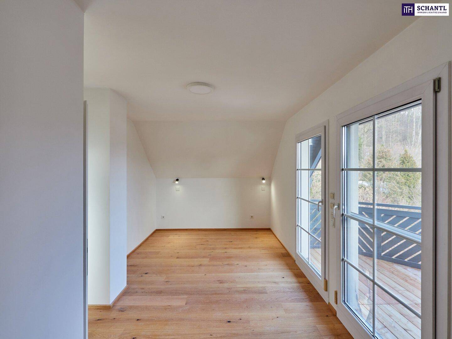 Geräumiges Schlafzimmer mit Holzboden und großen Fenstern, die auf einen Balkon führen.