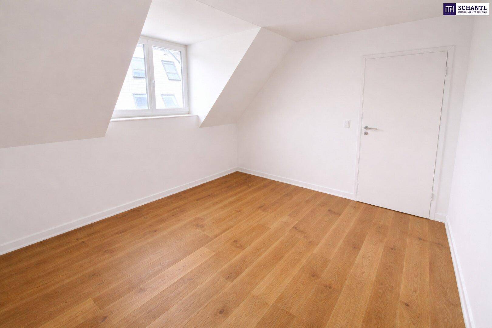 Helles Zimmer im Dachgeschoss mit schräger Wand, einem Fenster und neuem Holzboden.