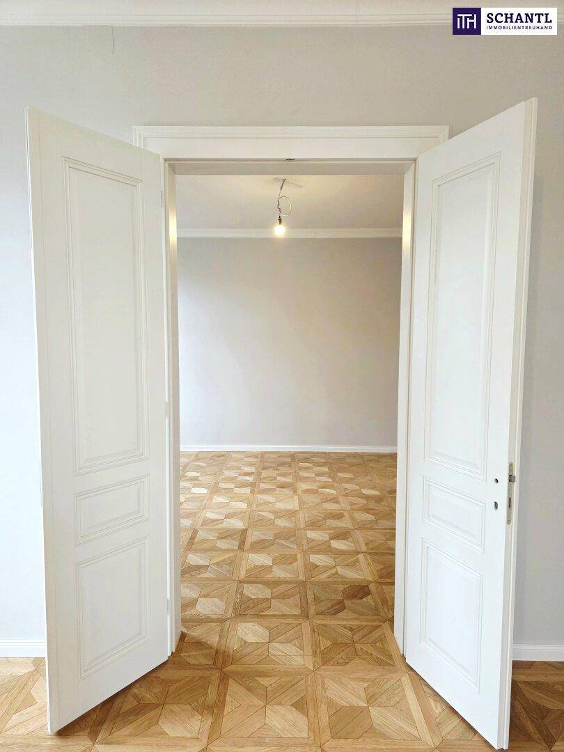 Klassische Doppeltüren öffnen sich zu einem weiteren Zimmer mit Parkettboden und hohen Decken.