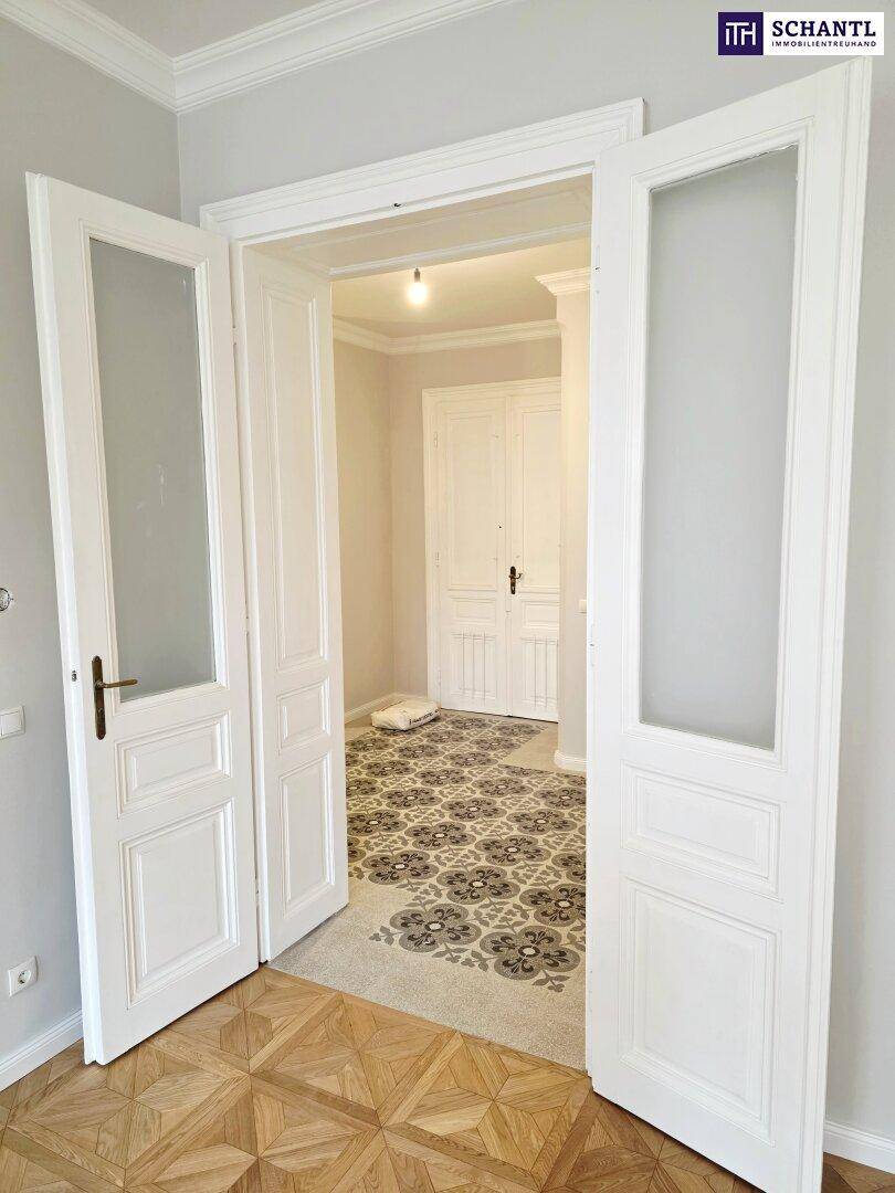 Doppeltüren mit Glaseinsätzen verbinden zwei helle Räume mit unterschiedlichen Bodenbelägen.