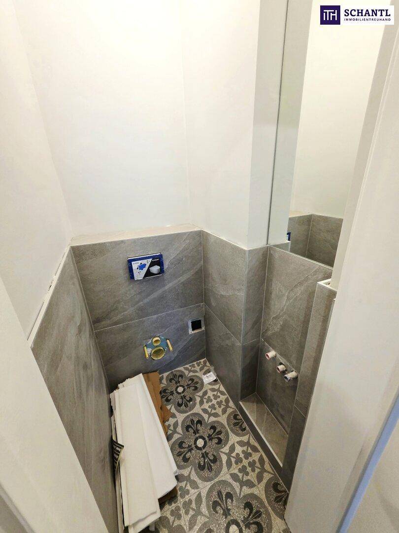 Badezimmer im Umbau mit modernen grauen Fliesen und vorbereiteten Anschlüssen für Waschtisch und Dusche.