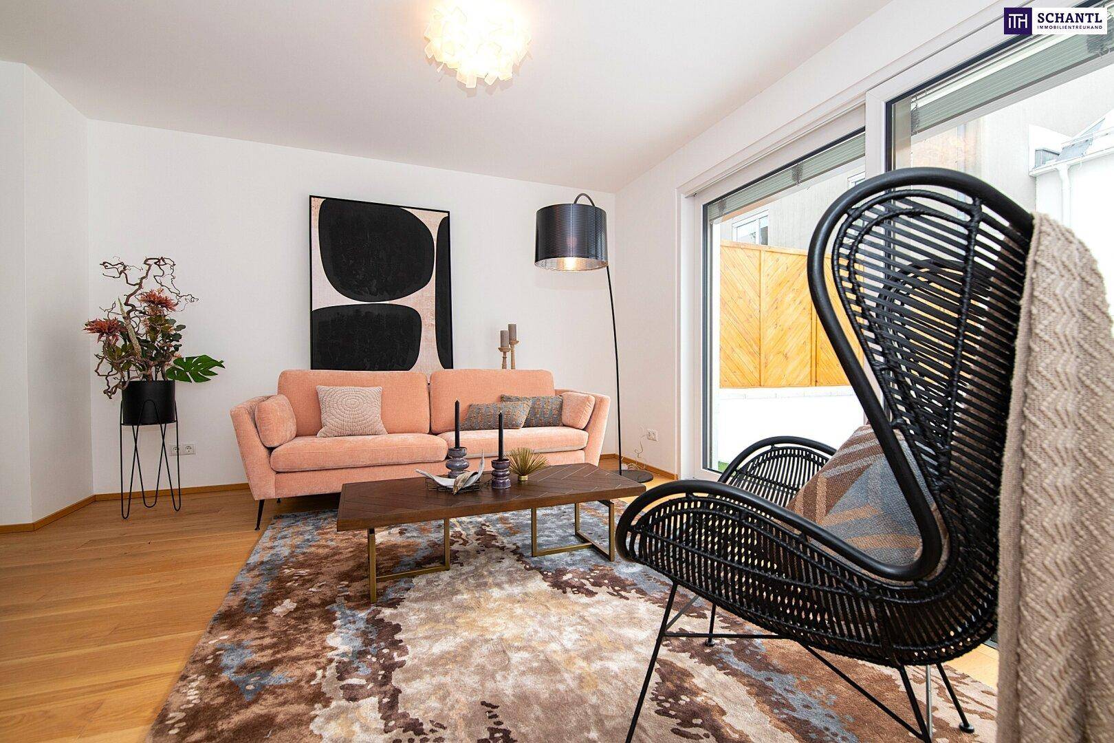 Helles Wohnzimmer mit bequemer Couch, Teppich und Zugang zur Terrasse durch große Fenster.
