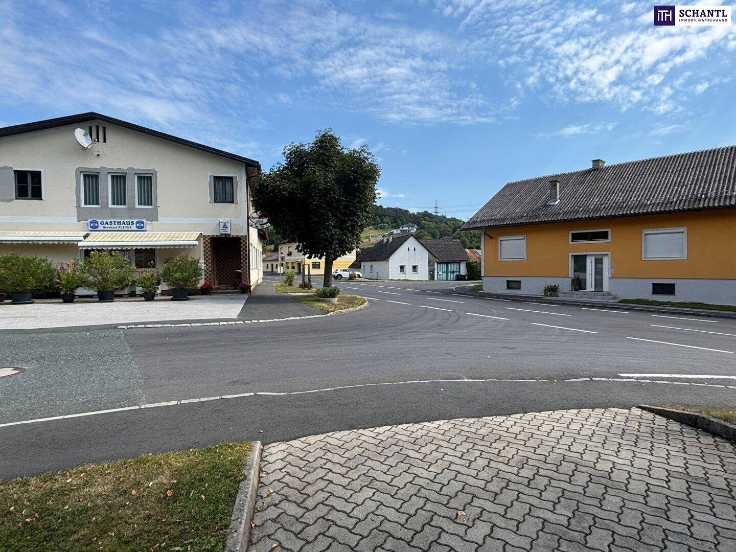 Blick auf die ländliche Umgebung mit Wohnhäusern, Straßen und grünen Hügeln im Hintergrund.