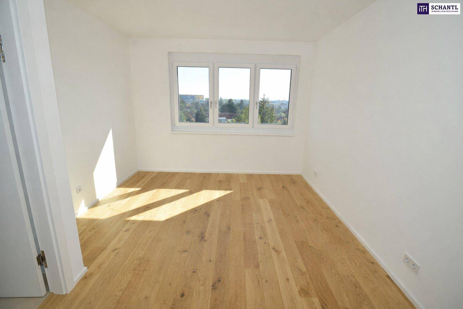 Helles Schlafzimmer mit Holzboden und Fenster mit Blick ins Grüne.