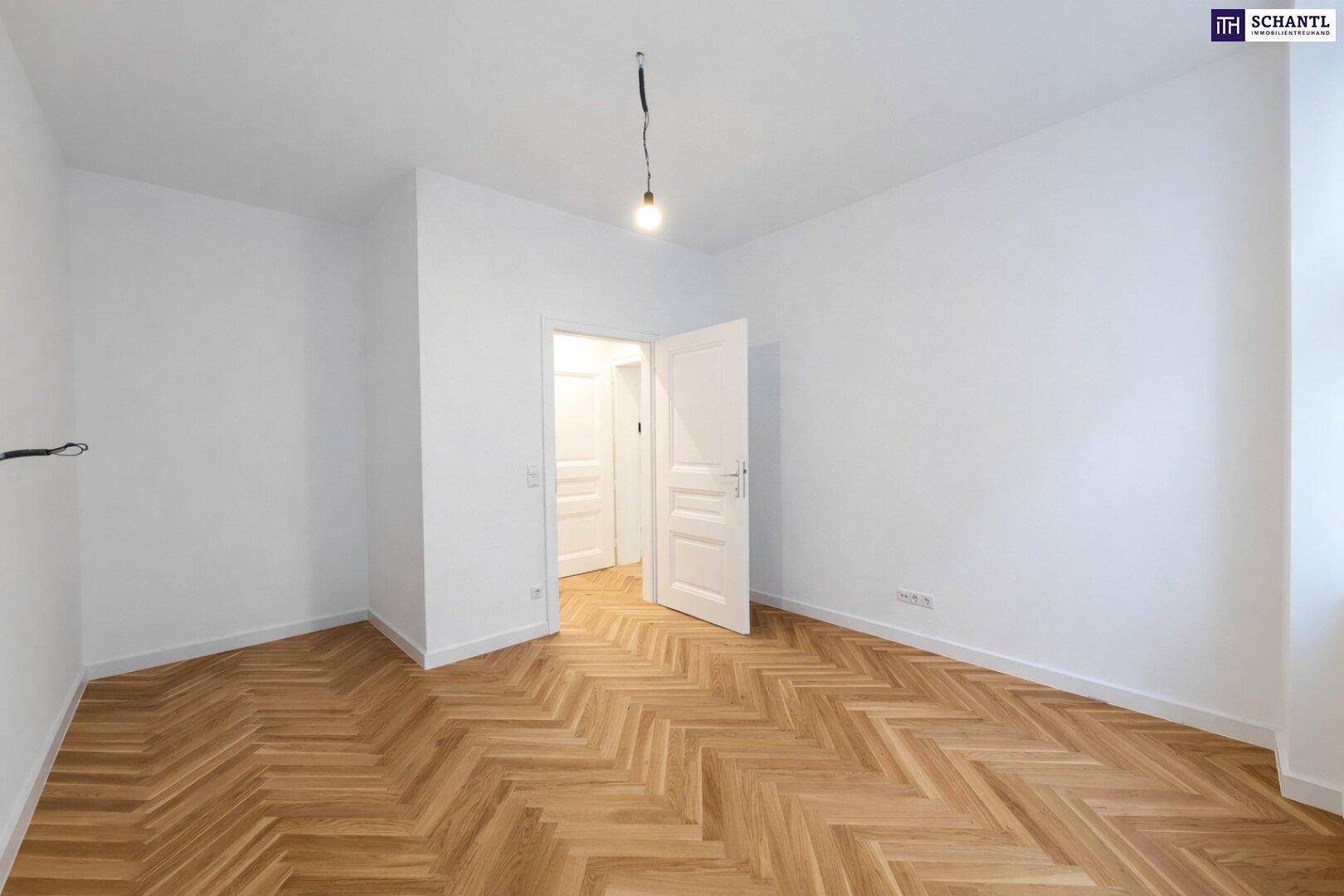 Leeres Zimmer mit Fischgrätparkettboden und weiß gestrichenen Wänden, mit Zugang zu weiteren Räumen.