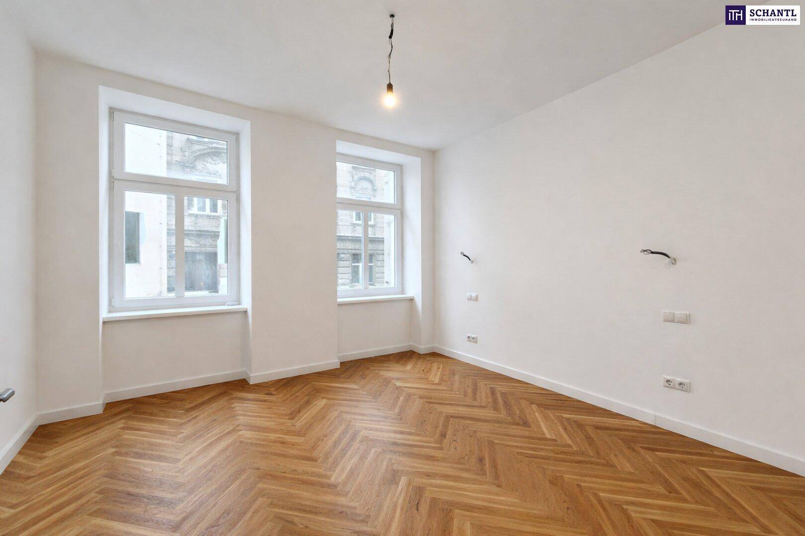 Geräumiges Zimmer mit Fischgrätparkett und zwei Fenstern, bietet viel natürliches Licht.