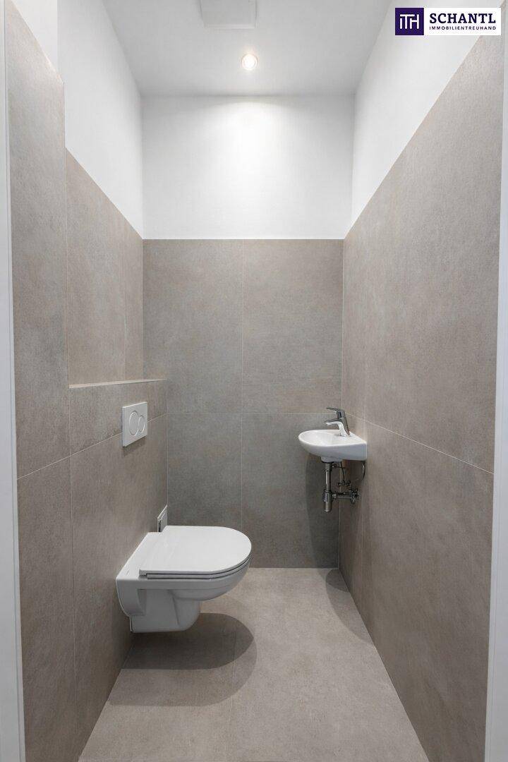 Separates Gäste-WC mit wandhängender Toilette, kleinem Waschbecken und grauen Fliesen.