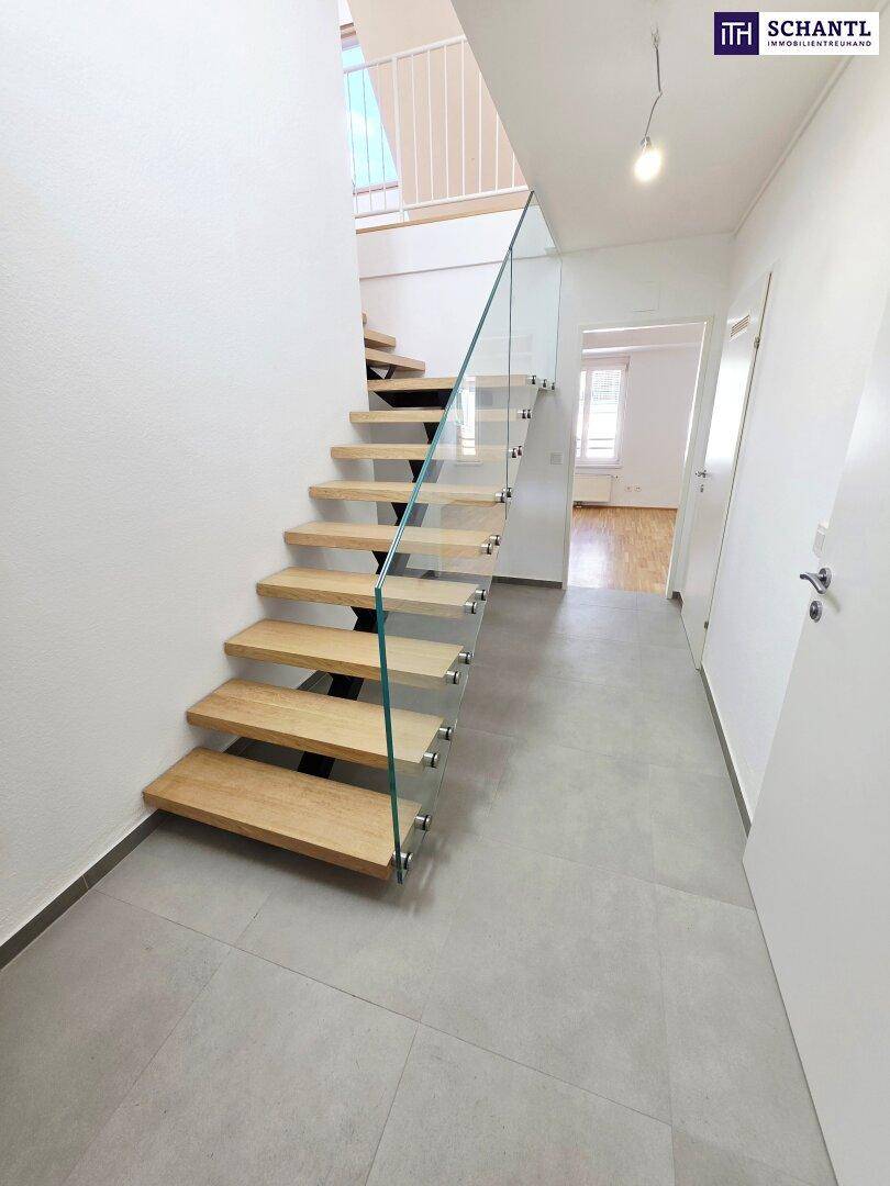 Moderne Holztreppe mit Glasgeländer und hellem Fliesenboden, die in die obere Etage führt.