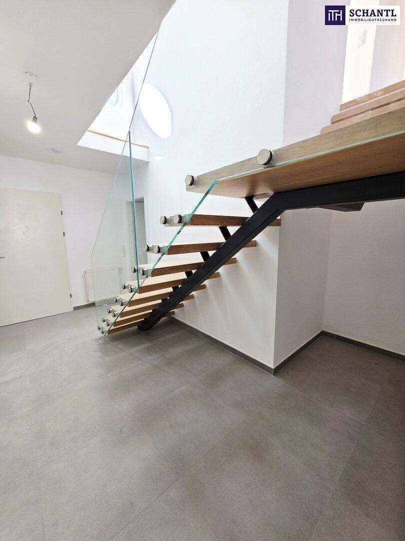 Moderne Treppe mit Holzstufen und Glasgeländer von unten gesehen, führt in die obere Etage.
