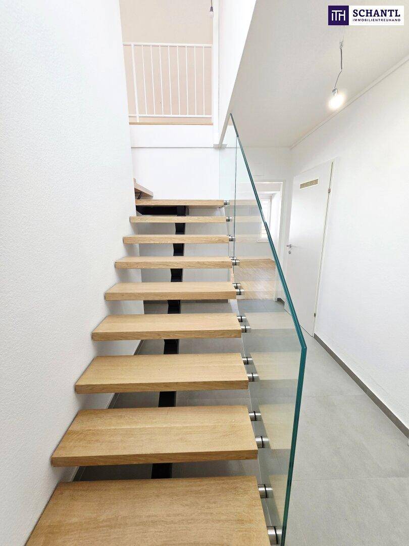 Moderne Holztreppe mit Glasgeländer und hellem Fliesenboden, die in die obere Etage führt.