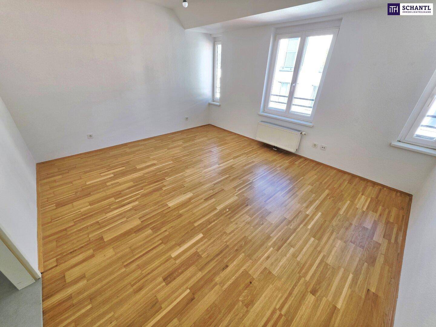 Helles Schlafzimmer mit Parkettboden und Blick auf die umliegenden Gebäude.