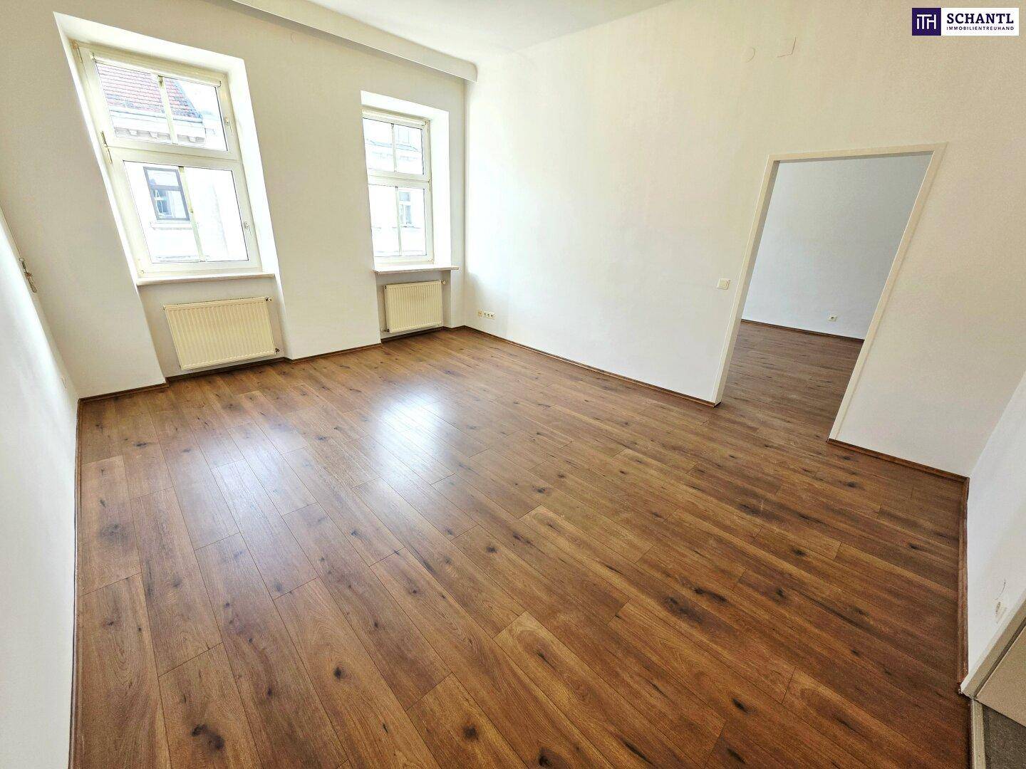 Helles, leeres Zimmer mit neuem Laminatboden und zwei Fenstern, bereit zur individuellen Gestaltung.