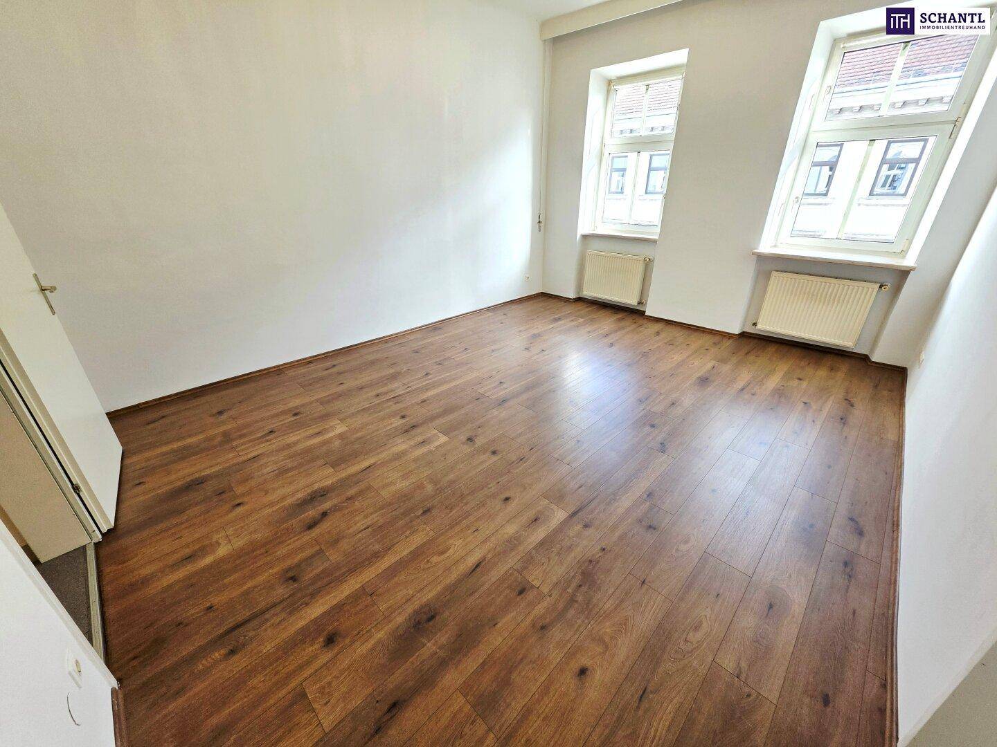Geräumiges, helles Zimmer mit Laminatboden und zwei Fenstern, ideal für Wohn- oder Schlafbereich.