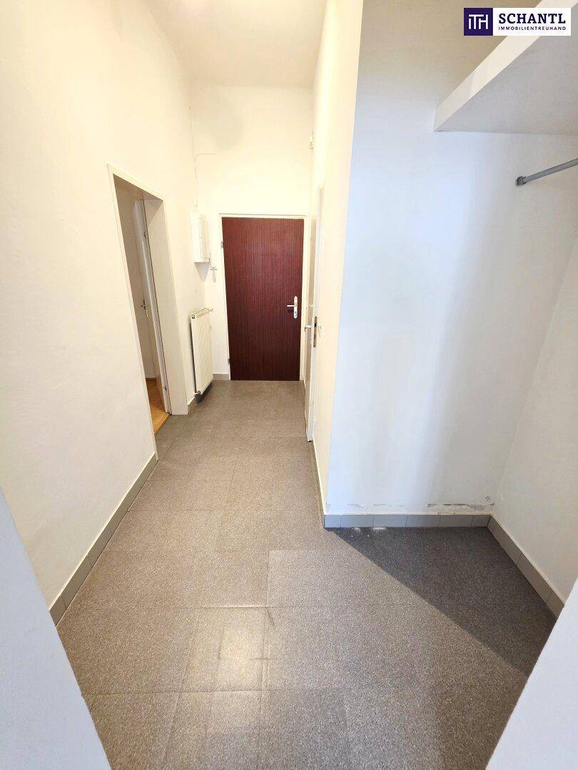 Heller Flur mit grauen Fliesen, der zu einer dunklen Tür und einem praktischen Abstellbereich führt.