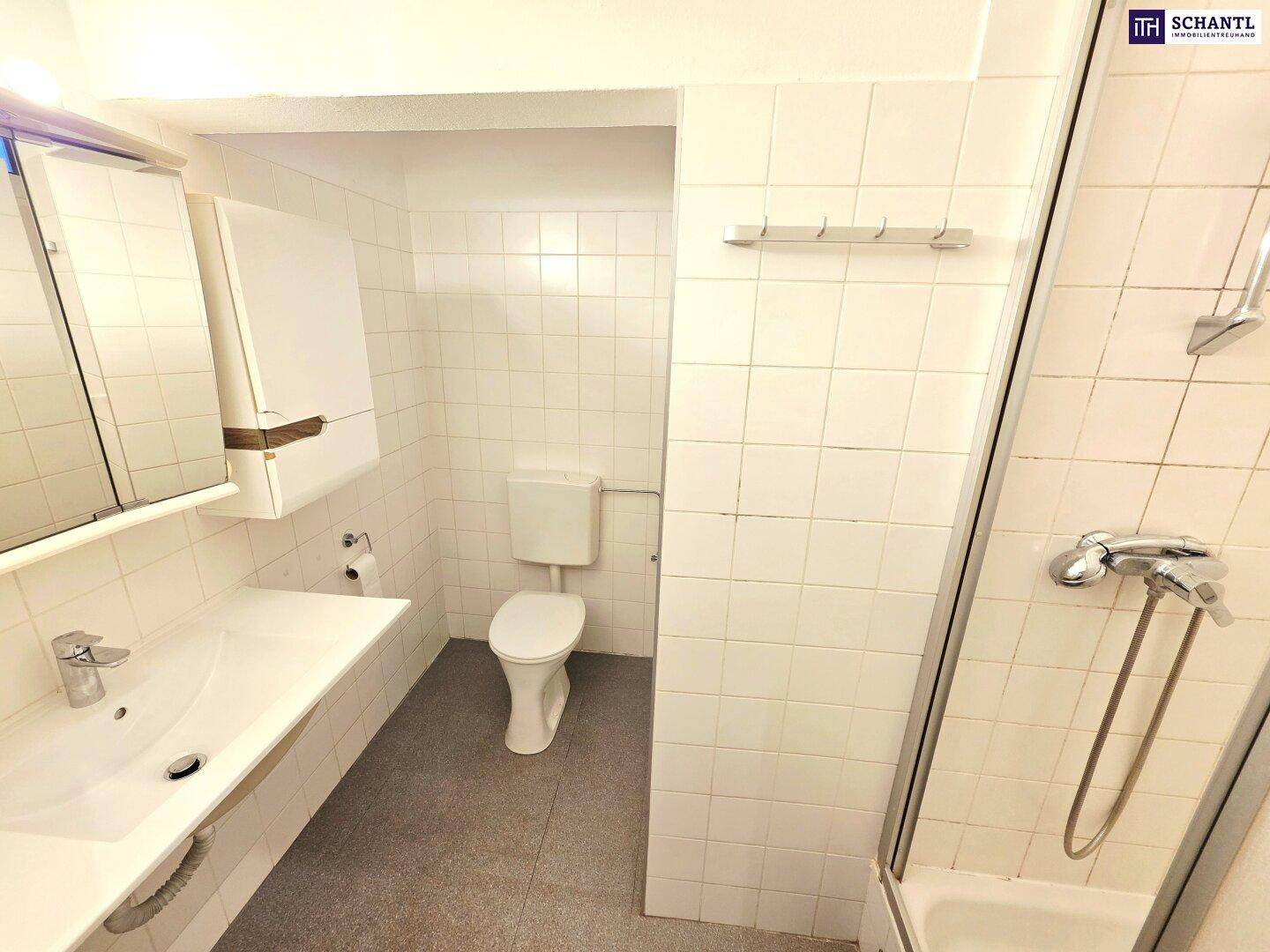 Helles Badezimmer mit weißen Fliesen, Waschbecken, Toilette und einer Duschkabine.