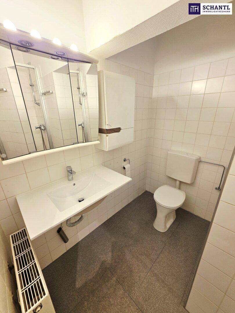 Funktionelles Badezimmer mit weißen Fliesen, Waschbecken, Toilette und einer Duschkabine.