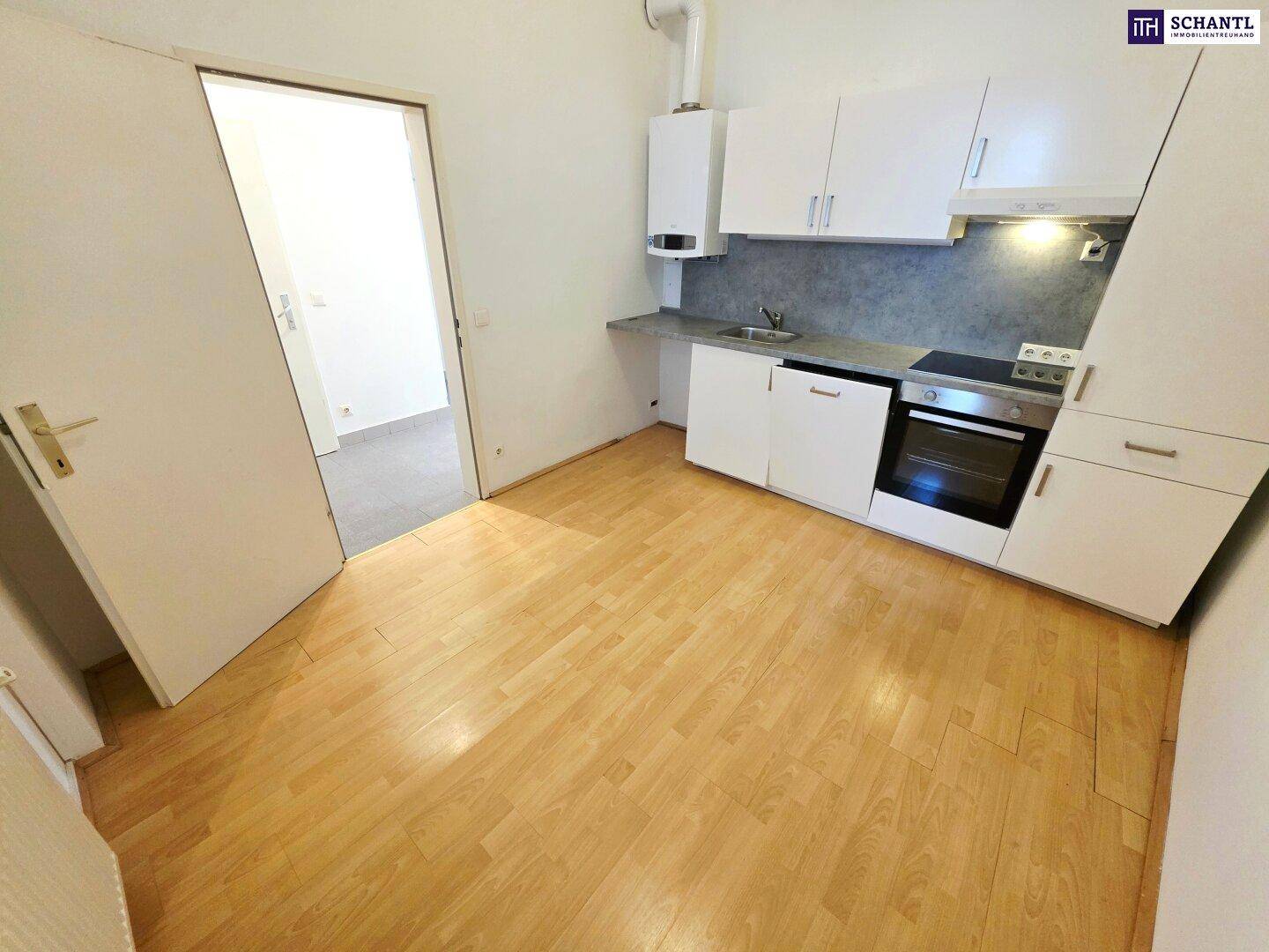 Kleine, funktionale Küche mit hellen Holzschränken, integriertem Ofen und Laminatboden.