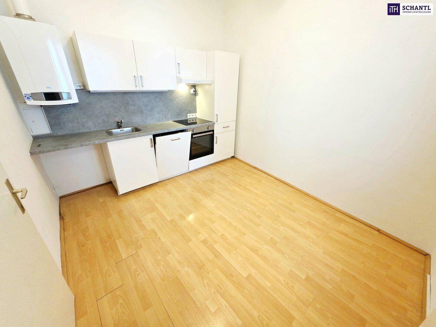 Kompakte Küche mit weißen Schränken, integriertem Kochfeld und Laminatboden, ideal für kleine Wohnungen.