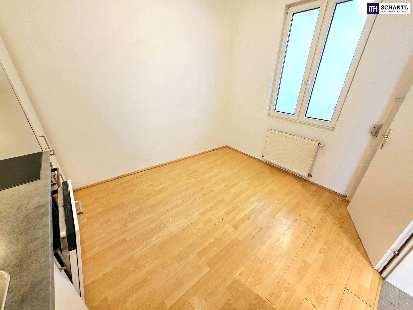 Helles Zimmer mit Laminatboden und Fenster, angrenzend an eine Küchenzeile.